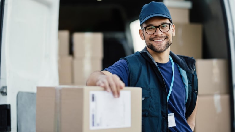 A professional smiling and standing next to cardboard boxes.