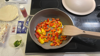 A pan on a stove filled with red bell pepper and bright yellow mango.