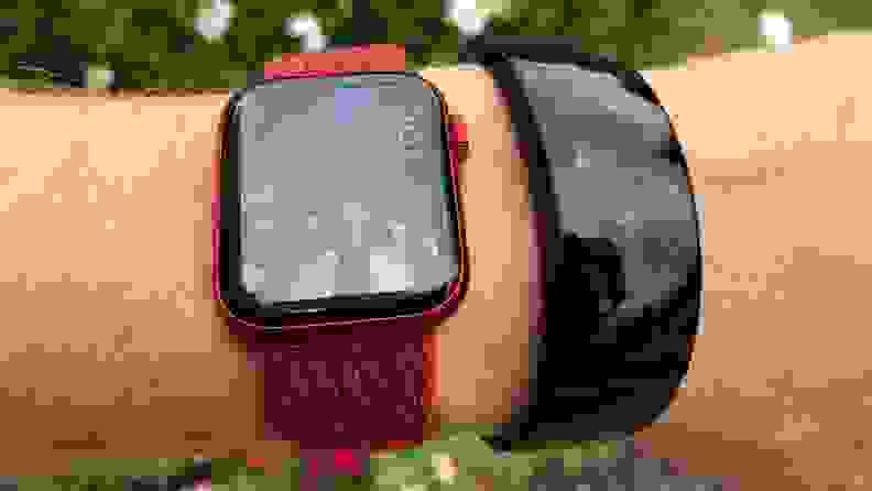 The all-black Amazfit X is shown outside next to an Apple Watch on a wrist with dulled colors in the sun across its curved OLED display.