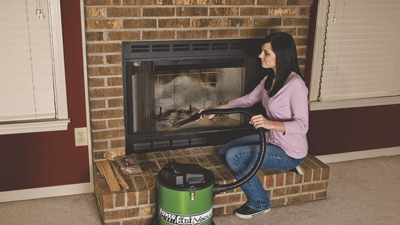 Woman using vacuum to clean fireplace.