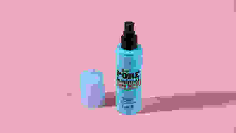 A turquoise bottle of makeup setting spray on a pink background.