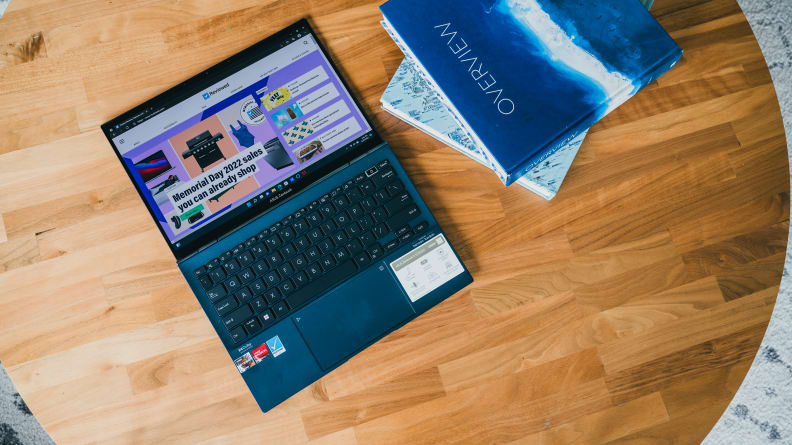 An open laptop lying flat on a table with books to its right side.