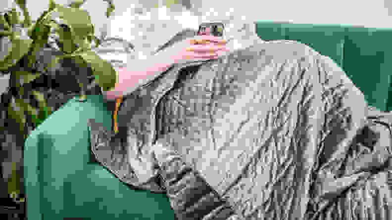 Person sitting on couch wearing blanket while looking at smartphone smartphone.