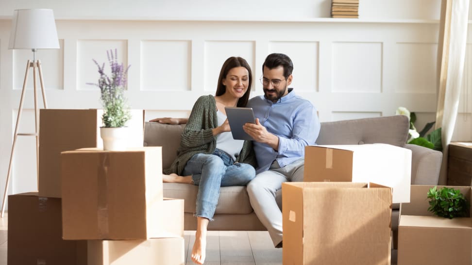 Couple sitting on couch with boxes surrounding them.