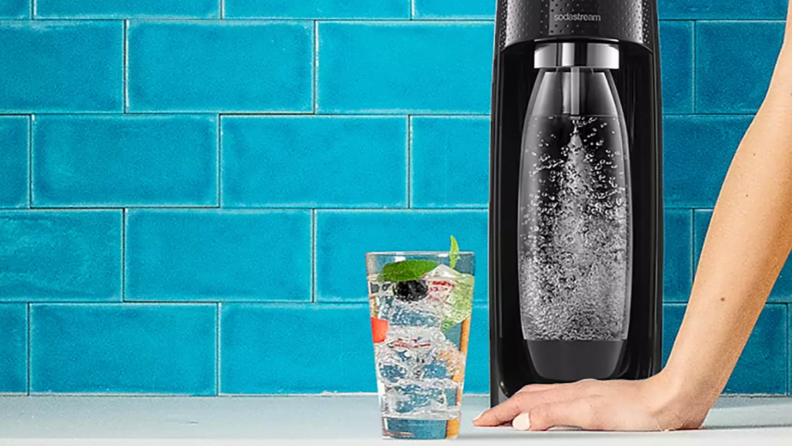 A SodaStream device sits on a kitchen counter next to a glass.