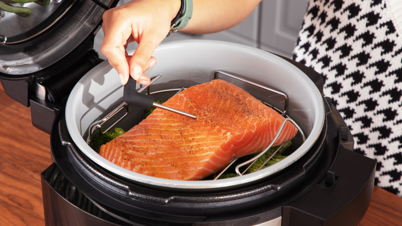 A person measures the temperature of a cooked piece of salmon inside a Ninja Foodi.