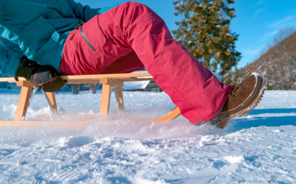 A model wearing snow pants glides across a frozen lake on a sled.
