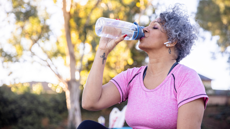 A person drinks from a plastic bottle while on a hike.