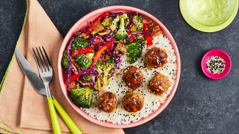 A pink bowl filled with rice, falafel, and vegetables.