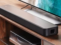 The Sony HT-S2000 soundbar sitting on a wood entertainment center, next to a TV.