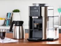 The De'Longhi True Brew on a countertop with a pot of coffee and cup of coffee next to it.