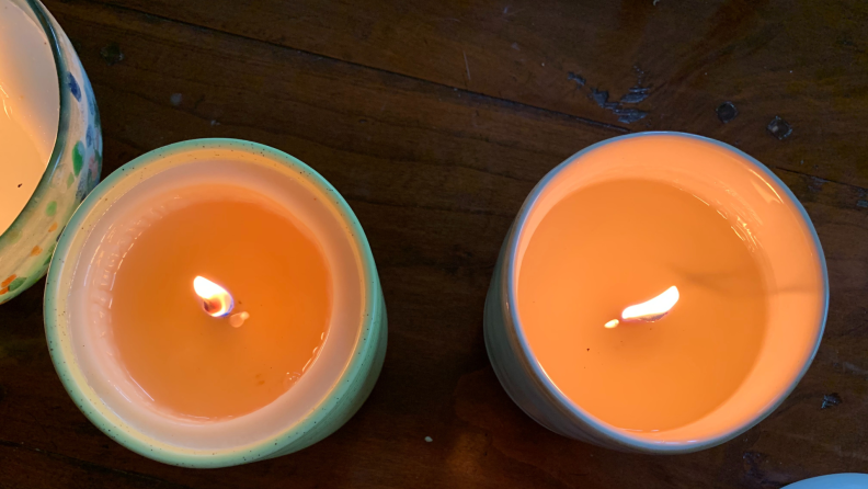 Two burning orange candles side by side sitting on top on table.