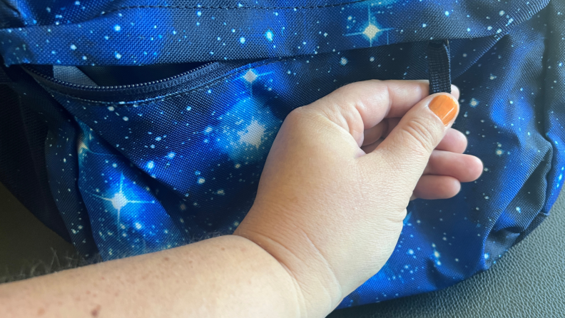 Person holding zipper tab in fingers on the Lands' End ClassMate XL backpack in Blue Galaxy Space color pattern.