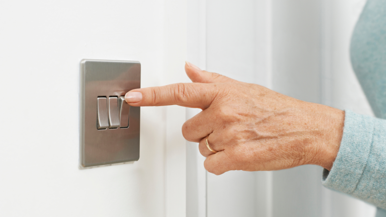 Hand of senior woman flipping toggle light switch.