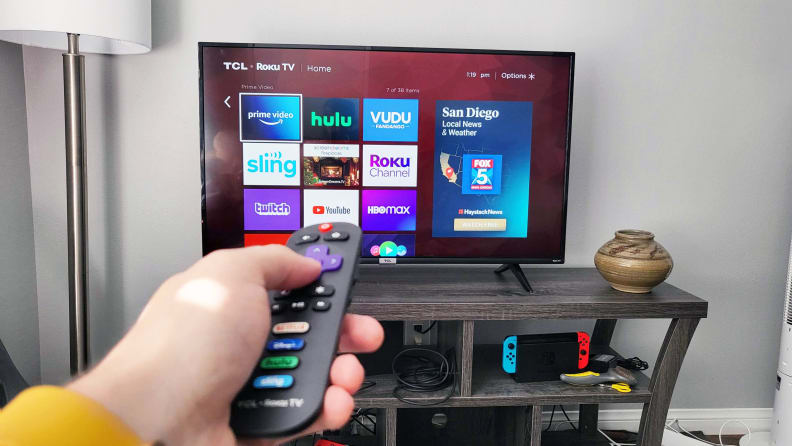 The TCL 4-Series displaying the home screen of its Roku smart platform in a living room setting