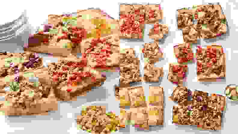 Various rectangular pizzas sliced into smaller rectangles, scattered across a marble surface.
