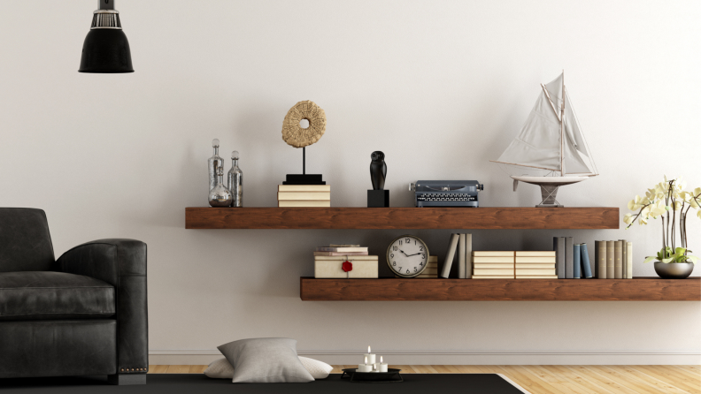 Two floating shelves in a living room hold a number of decor items, from books to a clock to a sailboat figurine.