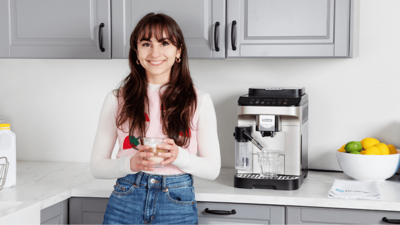 La escritora posa y sonríe frente al Delonghi Magnifica Evo con una taza de café en la mano.