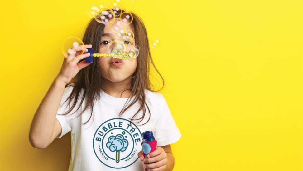 A girl blows bubbles on a yellow background.