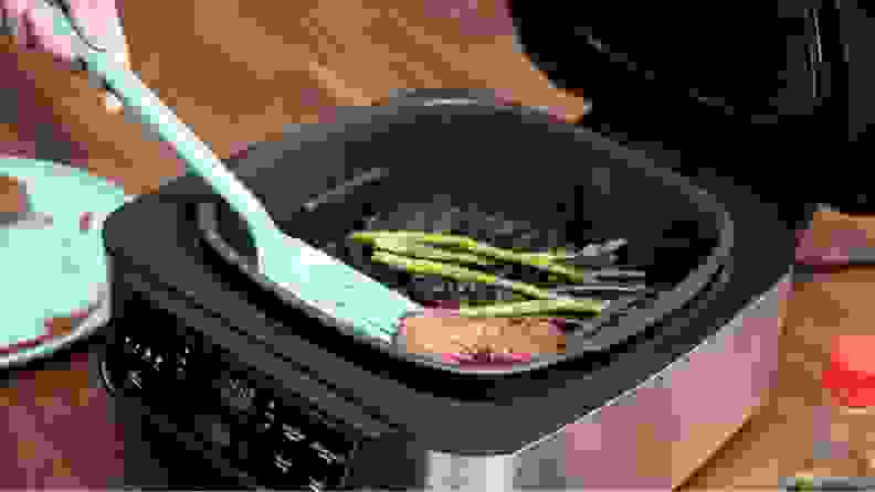 A burger and asparagus being cooked on an indoor grill.