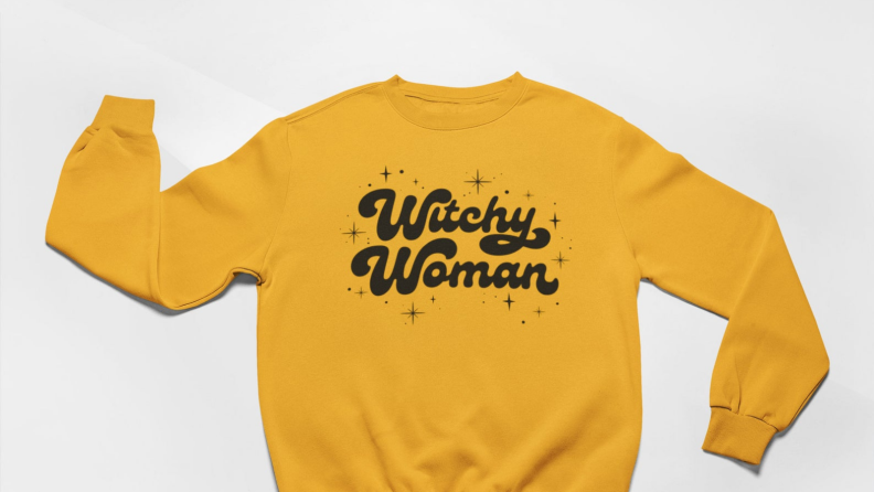 An image of a yellow sweatshirt with Witchy Woman written on it in black.