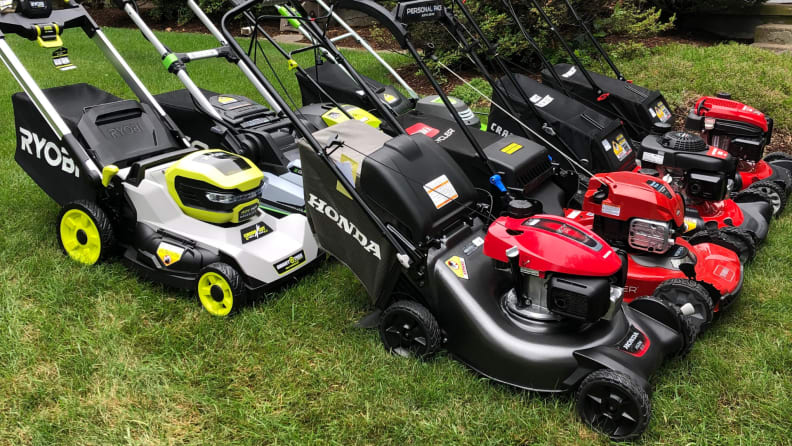 Eight lawn mowers sit on a green lawn.