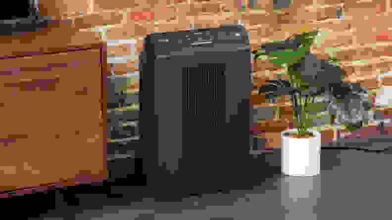 Black Winix 5500-2 air purifier on top of wooden floorboard in front of brick wall indoors.