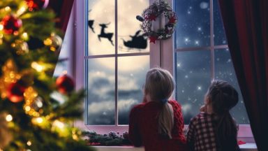Two children staring out the window looking at Santa fly by the moon.