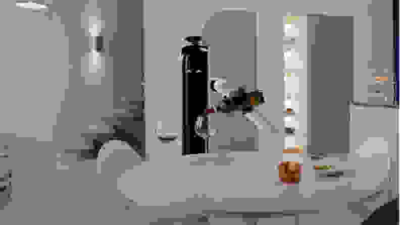 A slim, minimalistic robot (dubbed the Bot Handy) with crescent-shaped eyes and one mechanical arm pours a glass of wine.