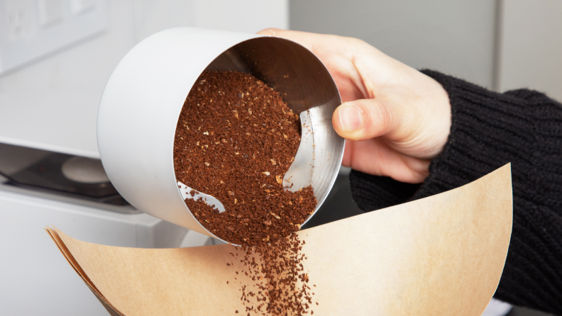 Person pouring finely ground coffee beans into paper cone.