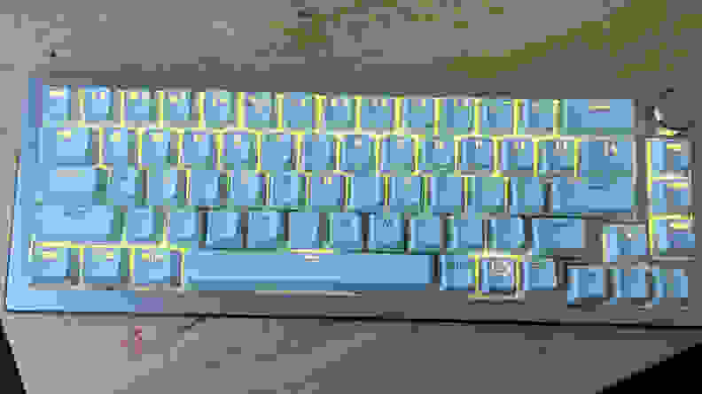 A keyboard with yellow glowing keys on top of a light brown desk