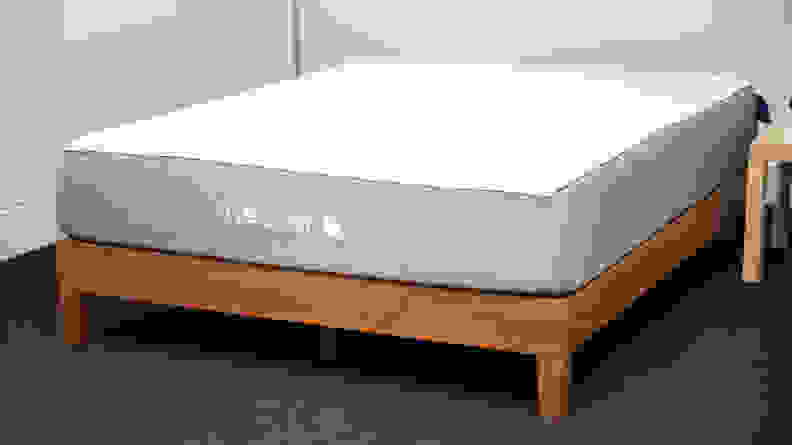 A bare Nectar mattress on a wood bed frame in a carpeted room with white walls