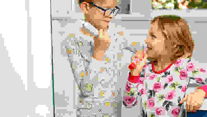 A boy and a girl wear pajamas and smile at one another while holding toothbrushes.
