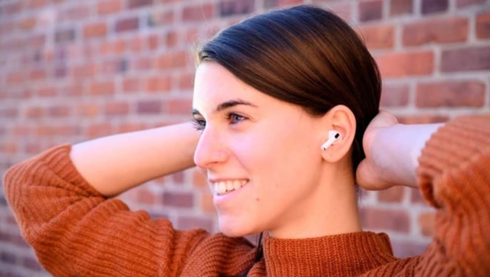 A woman leaning back against a brick wall wearing a pair of AirPods.