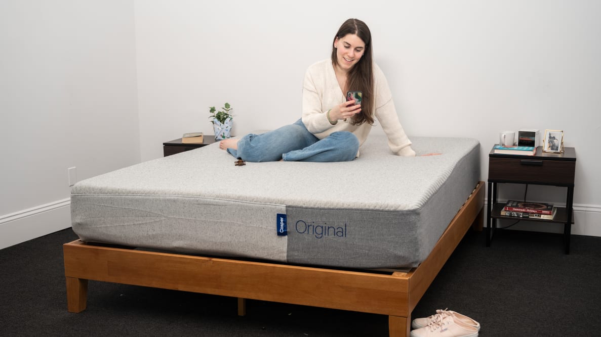 a woman sits on the Casper Original mattress looking at her phone in a bedroom.