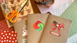 Homemade Christmas cards laying on top of decorative paper, stickers, washi tape, scissors