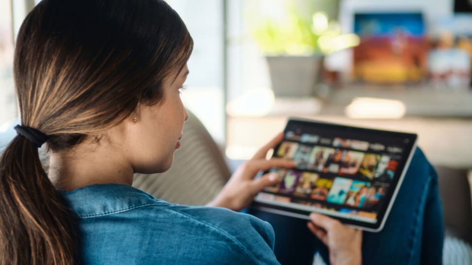 Person searching through streaming options on tablet while sitting.