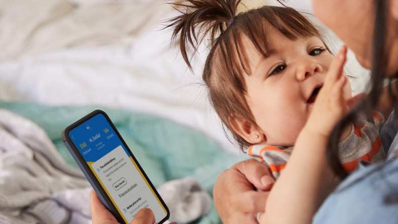 Woman ordering groceries on an app while holding a baby.