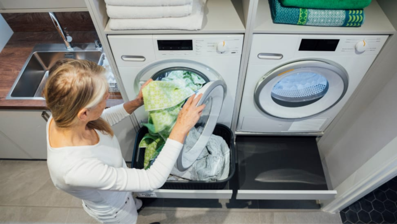A person puts a load of laundry into a washing machine.
