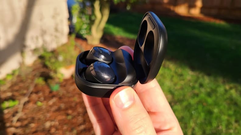Person holding black earbuds up outdoors.