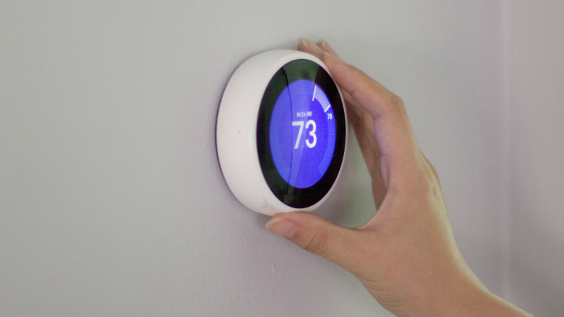 A hand turning the dial of a Nest smart thermostat.