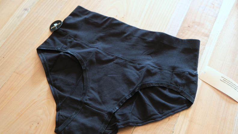 A photograph of a pair of black panties on a wooden background.