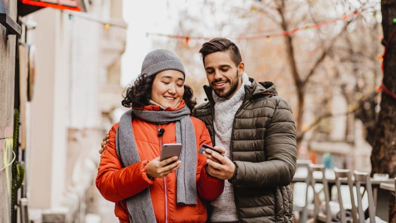 People smiling outdoors while making a purchase on smart phone.