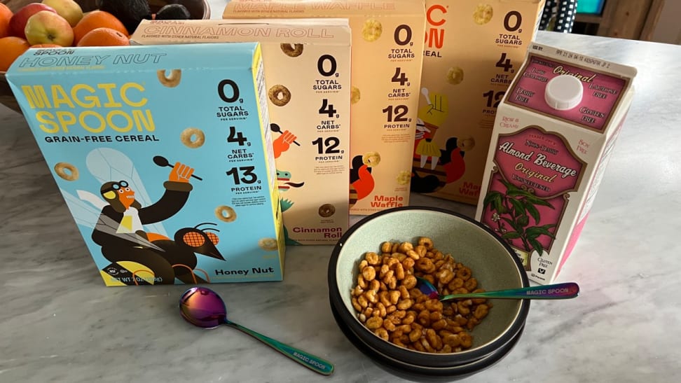 Boxes and bowls of Magic Spoon cereal on a marable counter with a half gallon of almond milk.