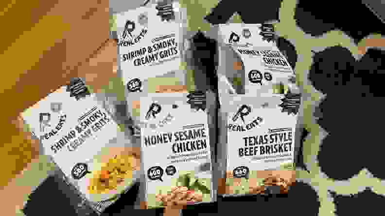 图片中有五包RealEats预制食品。从左起:奶油玉米粉虾，蜂蜜芝麻鸡，和德州风味的牛腩。