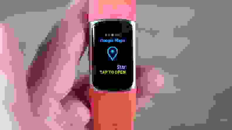 Person holding a Fitbit Charge 6 with an orange band has the Google Maps app on screen.