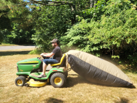 Person riding on lawn mower with the TerraKing 54 cubic foot Pro Leaf Bag on back.