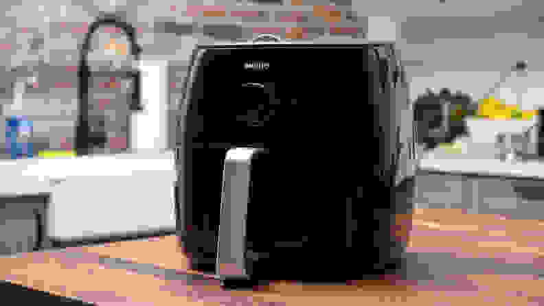 这Philips XXL air fryer sits on a kitchen counter. It has a silver handle in front of the black appliance.