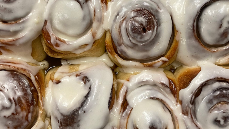 Eight cinnamon buns with icing is on display.