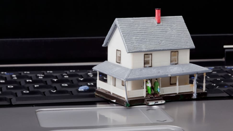 Miniature model home sitting on top of keyboard of laptop computer.